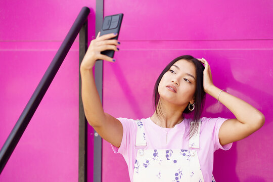 Asian woman taking selfie against pink wall