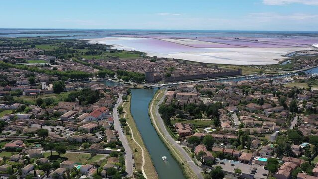 Boat in a canal along Aigues-Mortes medieval city aerial pink ponds full of salt France