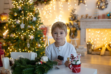 Cute preschool child, blond boy, making advent wreat at home in decorated Christmas room