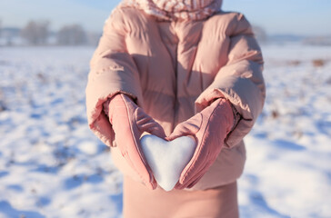 A stylish girl holds a heart made of snow in pink gloves. Selective focus.