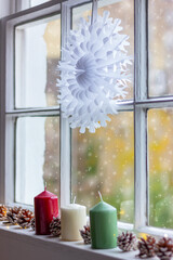 large paper snowflake, candles and cones on the window. winter, New Year and Christmas decorations