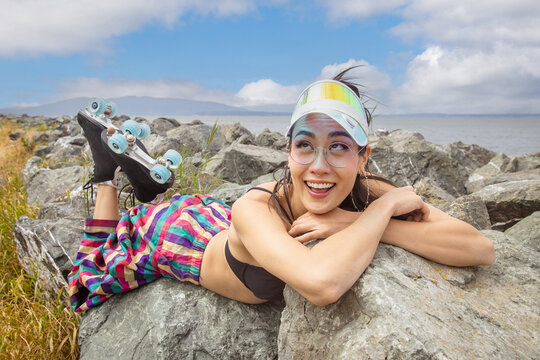 Funny Asian woman with her eyes crossed laying outside on a boulder rock near water