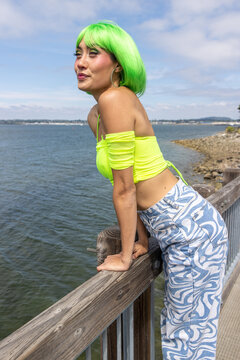 Pretty Asian woman with vibrant neon green hair looks at ocean water on a sunny summer day