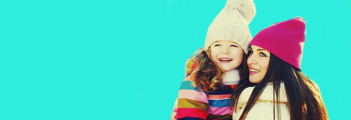 Winter portrait of happy smiling mother and little girl child looking away on blue background
