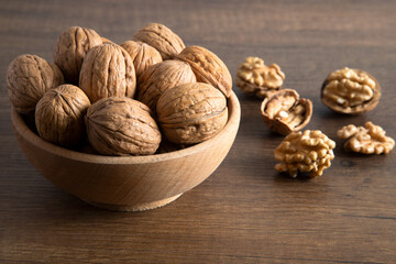 Bowl of walnuts and whole walnut kernels on wooden table