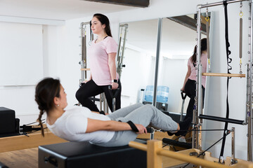 Fototapeta premium Positive young Latina practicing pilates stretching exercises on reformer at gym..
