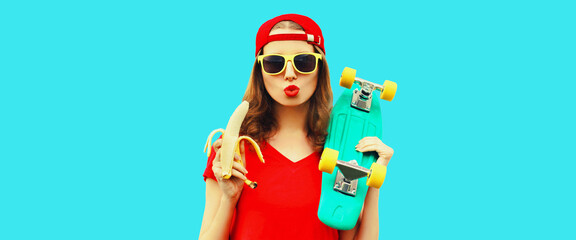 Portrait of stylish young woman blowing her lips with red lipstick holding banana and skateboard isolated on blue background © rohappy