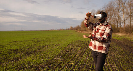 Young man standing in a wheat field at sunset in virtual reality glasses