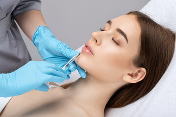 Obraz na płótnie Canvas Cosmetologist does injections for lips augmentation and anti wrinkle in the nasolabial folds of a beautiful woman. Women's cosmetology in the beauty salon.