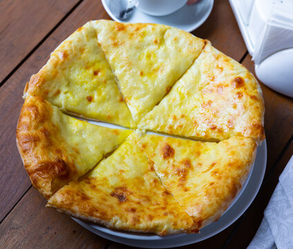 Upper view of freshly baked Imeretian khachapuri on wooden table. Traditional Georgian flatbread topped with sulguni cheese