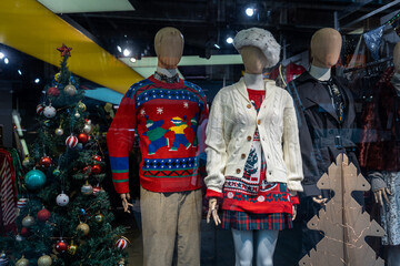 London, UK - November 30, 2022 shop window. Ugly Christmas sweaters on mannequins, a decorated Christmas tree.