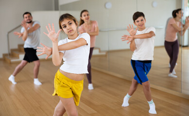 Portrait of positive pre-teen girl doing dance workout with her brother and parents during family class