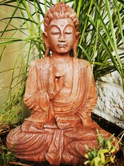 Vertical shot of a wooden Buddha sculpture near green plants
