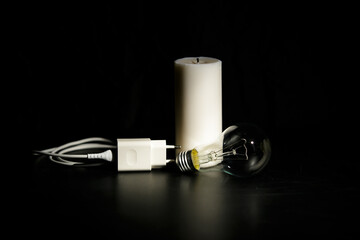 Blackout concept. Electric charger with cable near lighting candle on dark background.