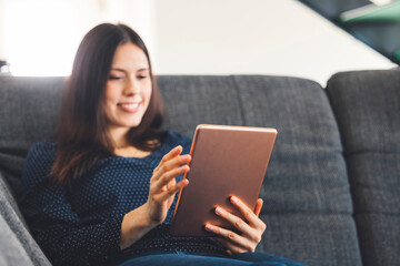 Smiling caucasian woman online shopping on her tablet while relaxing on the sofa