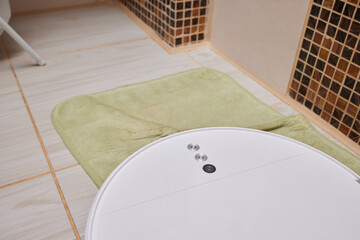 White robot vacuum cleaner on carpet in bathroom.