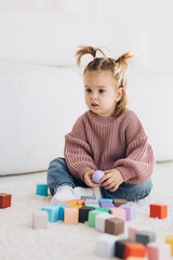 girl plays toys in living room. Montessori wooden toy folded pyramid. Circle, triangle, rectangle...