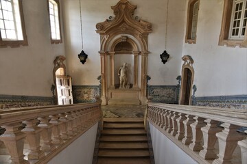 View from the top of the beige and white grand Rococo three-flight stone staircase at Colégio de São Jerónimo, Coimbra University, onto a recess with a marble statue, Coimbra, Portugal