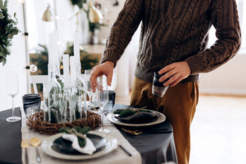 Obraz na płótnie Canvas man hands serving Christmas table setting in Scandinavian living room, close up view on table set event in dining room