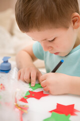 A cute baby writes a Happy New Year on a star cut out of paper. Preparation of decor and gifts for Christmas and New Year holidays. Close-up.