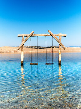 Empty swing in the water. Pebble beach on Adriatic coast of Croatia. Island Krk on background. Jadranovo village near Rijeka in Dalmatia, Croatia. Romantic wooden swing in transparent sea water.