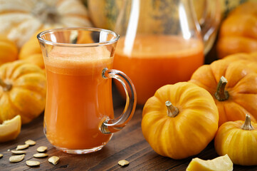 A glass cup of pumpkin juice. Pumpkins on kitchen table. Jug of pumpkin juice on background.