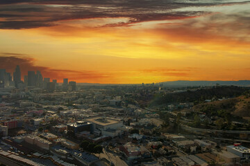 Fototapeta na wymiar aerial shot of the skyscrapers and office buildings in the city skyline over Los Angeles State Historic Park with lush green trees with powerful red clouds at sunset in Los Angeles California