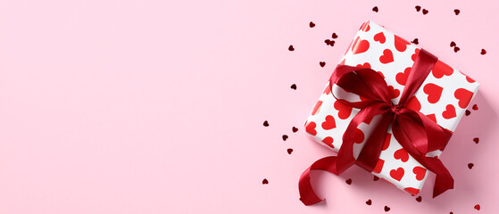 Gift box with red ribbon bow and confetti hearts on pastel pink background. Happy Valentines Day banner mockup, Mothers Day greeting card template.