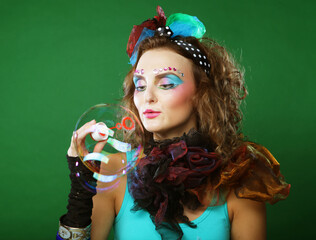Young woman with creative make-up blowing soap bubbles over green background. Doll style.