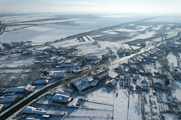 Top view of the highway and the parallel railroad. Snow-covered fields and houses. Countryside.