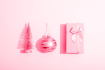 Gift box, Christmas ball and fir tree toy on pink background with sharp shadows. Minimal composition. Top view, flat lay
