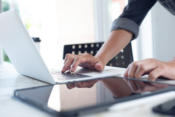 Closeup of business man hand typing on laptop computer and using digital tablet pc on table at home office. Designer working on design project, work from home, paperless office