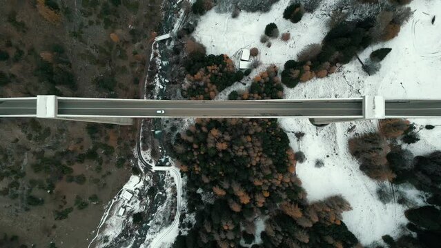 A bridge in the mountains filmed from above. Cars drive over the span and a river flows under the bridge. It is autumn and the landscape is covered with snow. Aerial Shot Ganterbr&uuml;cke