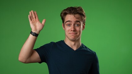 Waving and smiling, confused young man 20s posing isolated on green screen background in studio. People lifestyle concept.