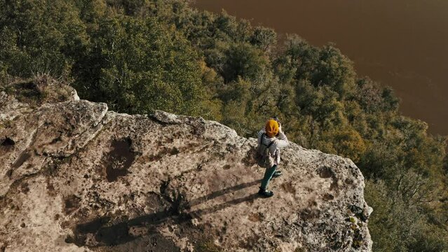 Drone shot at the edge of a cliff from behind a woman takes pictures and looks at the landscape