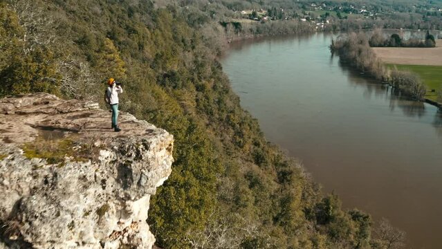 Aerial view from away of a woman in nature taking photos at the edge of a cliff, the landscape is cultivated and wild