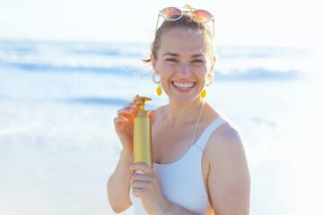 Portrait of happy elegant woman in beachwear at beach using spf