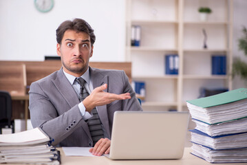 Fototapeta premium Young male employee unhappy with excessive work in the office