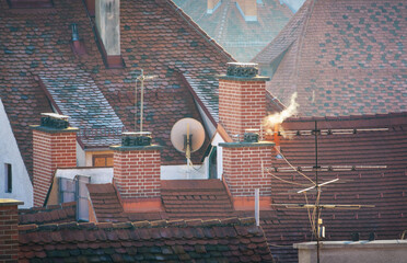 White smoke from a brick chimney against the background of tiled roofs