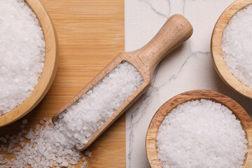 Wooden board with natural sea salt in scoop and bowls on white marble table, flat lay