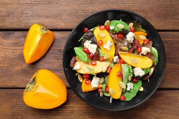 Delicious persimmon salad with pomegranate and spinach on wooden table, flat lay