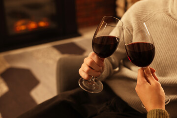 Lovely couple with glasses of wine resting together near fireplace at home, closeup
