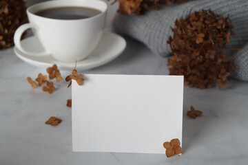 Dried hortensia flowers, blank card and cup of hot drink on white marble table, closeup