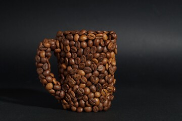 Cup made of coffee beans against black background