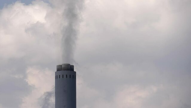 Single tall industrial smoke stack chimney pours smoke into cloudy sky