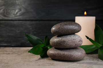 Stacked spa stones, bamboo and candle on wooden table. Space for text