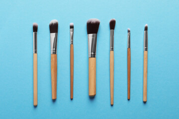 Different makeup brushes on light blue background, flat lay