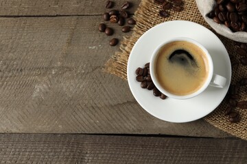 Cup of aromatic coffee and beans on wooden table, flat lay. Space for text