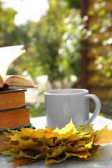 Naklejka na ściany i meble Yellow maple leaves, books and cup of tea on light gray table. Autumn atmosphere
