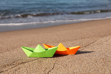 Fototapeta na wymiar Bright color paper boats on sandy beach near sea